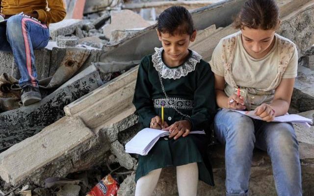 Children write in notebooks by the rubble of buildings destroyed by Israel near a tent being used as a make-shift educational center for primary education students in Jabalia in the northern Gaza Strip, Sept. 8, 2024. (AFP Photo)